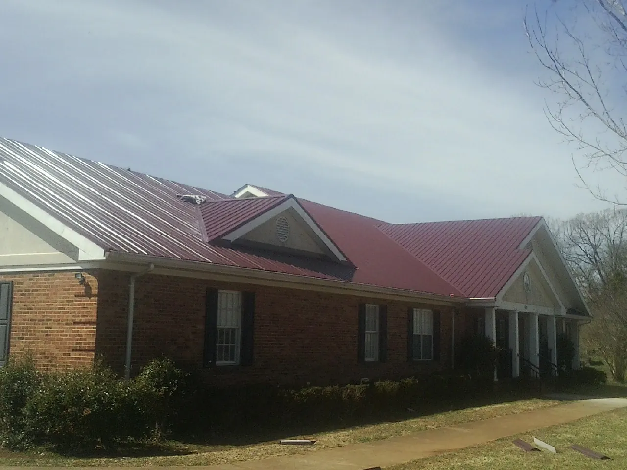 Red metal roof with gabled entries on a long brick building, from a Hail Damage Roof Repair job in Garland